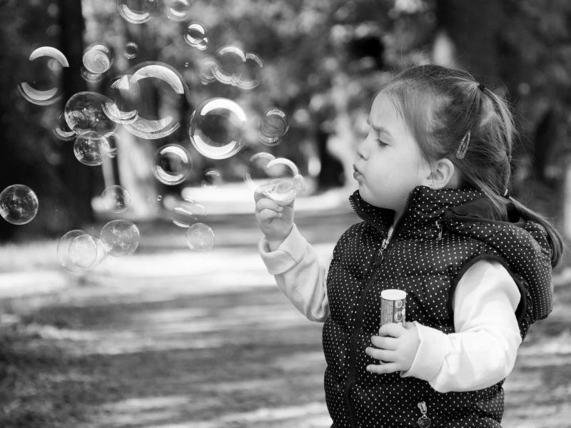 Female child blowing bubbles in a path lined with trees