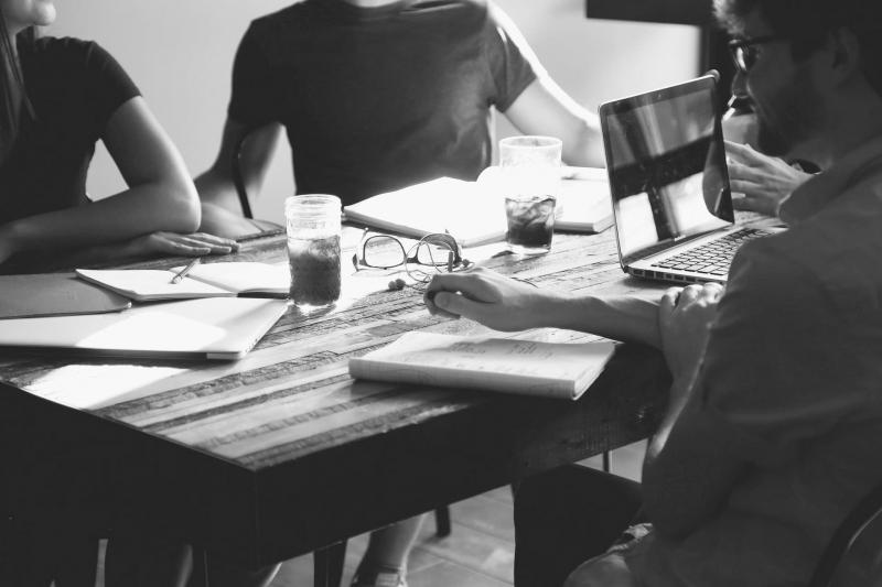 Four people sitting around a wooden table with notepads in front of them