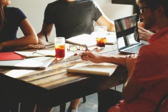 Four people sitting around a wooden table with notepads in front of them